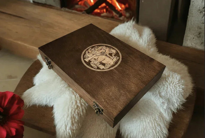 Handcrafted mahogany archive case with engraved Australian $1 coin logo, displayed on a white fur throw by a warm fireplace in a luxury interior.